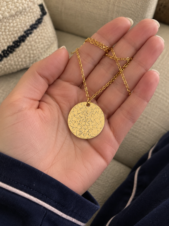 [TESTE] AI-generated mockup: round gold star map necklace in a hand. Not a customer photo.